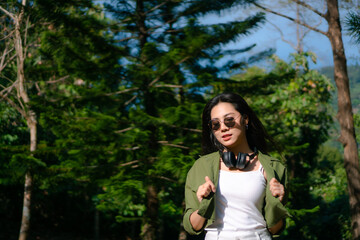 Naklejka premium portrait photography of girl with headphone,beautiful girl wearing sunglasses in the park,green pine trees as background