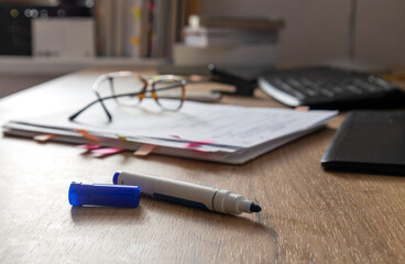 Closeup of blue marker for grammar correction.Pile of text paper,glasses,keyboard,tablet, stack of...