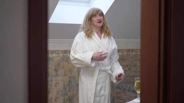 Joyful Carefree Caucasian LGBTQ Trans Woman Spinning In Bathroom Smiling Enjoying Happy Day At Home. Portrait Of Relaxed Gender-fluid Queer Person In White Bathrobe Resting Indoors. Self-perception