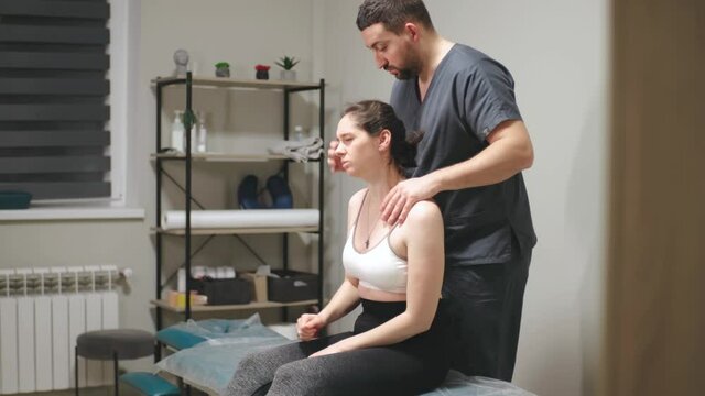 Professional male chiropractor, physiotherapist treating female patient in rehabilitation center