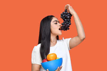 foodie girl wearing white t-shirt holding fruit bowl and eating grapes bunch indian pakistani model