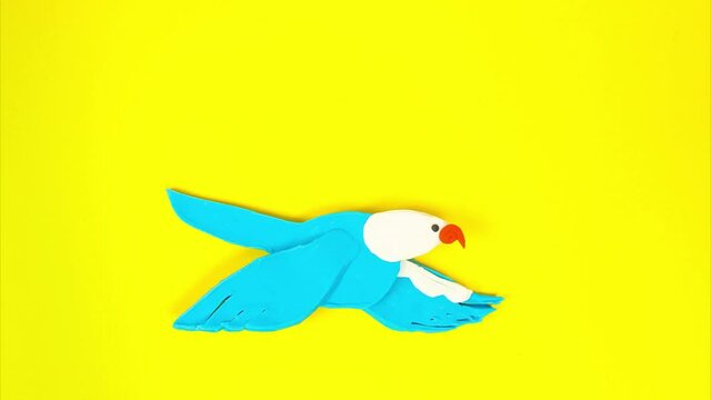 Plasticine bird in flight using the stop motion technique. Funny cartoon bird flaps its wings creating the illusion of flight on a yellow background