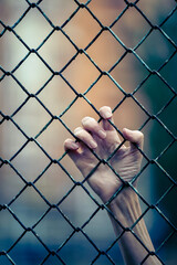 Dramatic view of a hand clutching a wire mesh fence