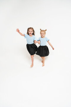 Two children are happily running. Happy and carefree childhood. Girls in identical T-shirts and skirts. The girl waves her hand and laughs.