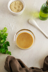 Tahini in a glass bowl with ingredients and herbs on a light background. The process of preparing a traditional Asian sauce. Levantine cuisine concept.
