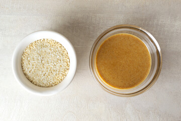 Tahini in a glass bowl with sesame seeds in a white bowl on a light background. Traditional Asian sauce for making hummus. Levantine cuisine concept. Vegan food.