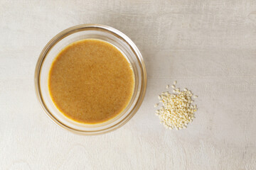 Tahini in a glass bowl with sesame seeds on a light background. Traditional Asian sauce for making hummus. Levantine cuisine concept. Vegetarian food. Copy space. Top view.