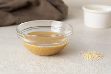 Tahini in a glass bowl with sesame seeds and a brown napkin in your home kitchen. Traditional Asian sauce for making hummus. Levantine cuisine concept. Horizontal orientation.