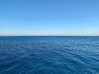 Blue sky and calm sea horizon. In the frame, half of the sky, half of the sea. Background texture: blue sky and clear water.