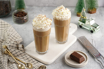 Two tall glasses with cold coffee drink frappe - iced cappuccino with whipped cream on a marble board and christmas ornaments and decoration