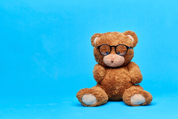 vision, school and childhood concept - brown teddy bear in glasses over blue background
