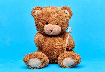 dental care, health and childhood concept - brown teddy bear with toothbrush over blue background