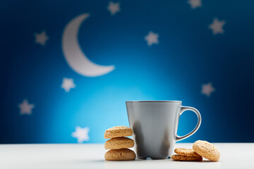 bedtime, sleeping and diet concept - close up of coffee cup and oatmeal cookies over moon and night stars on blue background