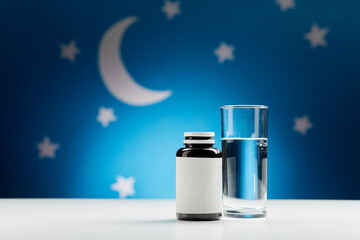 sleep disorder, bedtime and sleeping concept - close up of glass of water and soporific medicine...