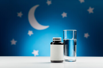 sleep disorder, bedtime and sleeping concept - close up of glass of water and soporific medicine over moon and night stars on blue background