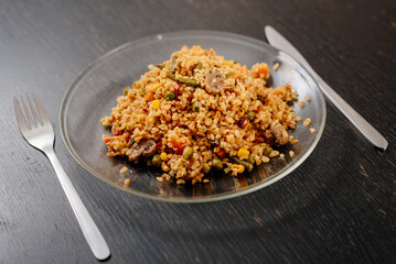 Bulgur with vegetables and mushrooms on a glass plate. Vegetarian food - wheat groats with vegetables and mushrooms.