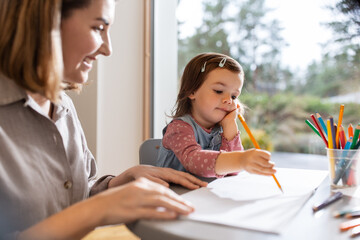 family, motherhood and leisure concept - mother spending time with her little daughter and drawing at home