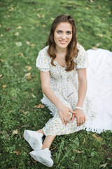 Tender young woman in beautiful dress sitting on the grass Happy brunette with disability enjoying summer weather during leisure walk at green park.