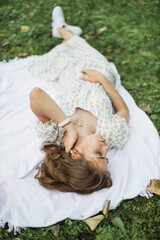 Fototapeta premium Portrait of young woman with physical disability in stylish summer dress smiling sincerely in camera at green park. Female person who lies on the green grass enjoying summer weather outdoors.