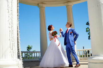Bride and groom in gazebo near the white columns in a sunny summer day in the city park