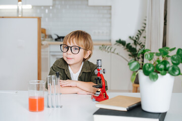 Adorable little boy in glasses sitting behind the table in front microscope