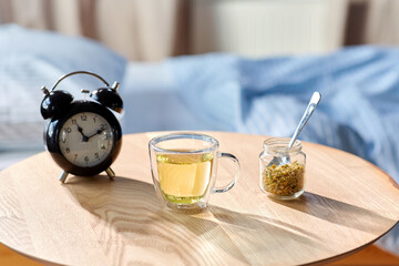 sleep disorder, bedtime and morning concept - close up of alarm clock and cup of relaxing chamomile tea on night table at home