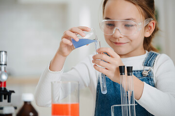 Smiling girl doing home science project, pouring liquid into a flask
