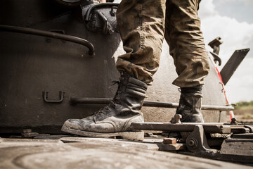 Legs of a soldier standing on metal tank, on a battlefield. Wearing military boots and woodland...