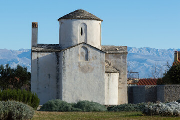 Fototapeta na wymiar Nin, Croatia - Famous monument, church of Holy Cross and Velebit mountains in the background; preserved pre-romanesque architecture
