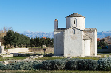 Fototapeta na wymiar Nin, Croatia - Famous monument, church of Holy Cross and Velebit mountains in the background; preserved pre-romanesque architecture