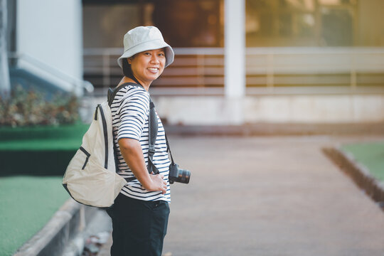 Asian woman traveling and taking pictures outdoors city streets, Asian female happy smiling backpacker using camera to take image on city walk streets, business travel concept