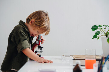 Side view little boy doing science project, looking through the microscope