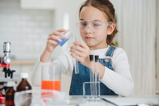 Cute focused girl doing home science project, pouring liquid into a flask