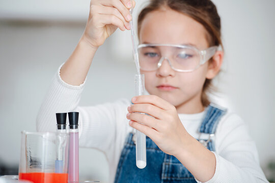 Focused girl doing science project, adding liquid in pipette with a white salt powder on the bottom. Trying to move slowly and precisely. Behind a table. Focus on her hands. - Powered by Adobe