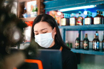 Asian young adult owner gen z young woman is wearing protective face mask standing at a counter bar in coffee shop cafe.  Open after lockdown quarantine. Social distance in new normal life concep