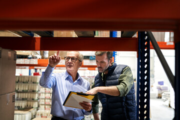 Two caucasian men in mature age discussing over documents together in warehouse