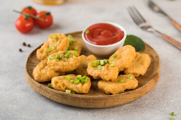 Golden chicken nuggets in a wooden plate, sprinkled with green onions and a lemon wedge. Pub menu