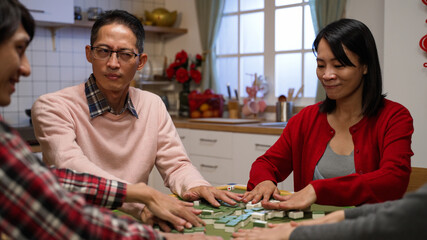 mother giving eye gestures to the father who is looking at other family member suspiciously while they are playing mahjong together at home during spring festival