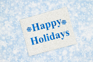 Happy Holidays greeting on silver greeting card on blue snowflakes