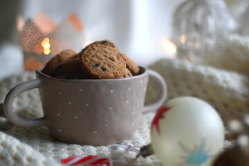 Bowl of cookies, soft knitted blanket and colorful Christmas ornaments at home. Selective focus.