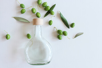 Top view of a glass bottle and a branch with olive on a white background. Mediterranean concept, botanical arrangement.Vacation concept.