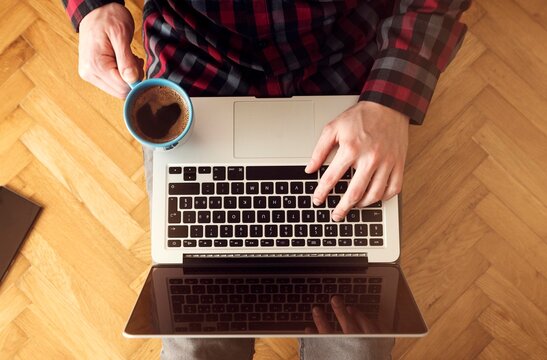 Top view of man using laptop and holding cup of coffee