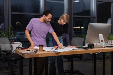 Fototapeta premium young interracial colleagues looking at blueprint on desk.