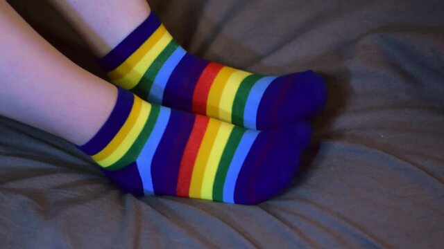 Wearing rainbow colored socks sitting in bed and jiggling the feet. Comfortable and funny piece of clothing