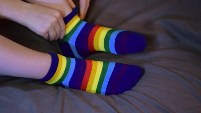 Putting on rainbow colored socks sitting in bed and jiggling the feet. Comfortable and funny piece of clothing