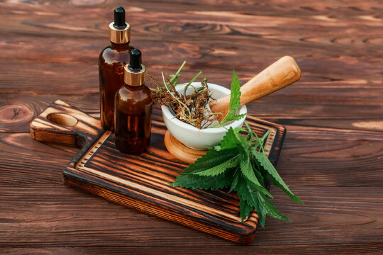 Fresh common nettle, stinging nettle or nettle leaf, or just a nettle root in ceramic mortar and pharmacy bottle with pipette. Ingredients for production of alternative medicine and homeopathic pills.