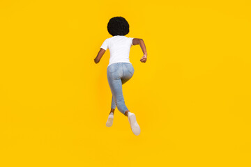 Fototapeta na wymiar Full length photo of adorable shiny dark skin woman dressed white t-shirt running fast jumping isolated yellow color background