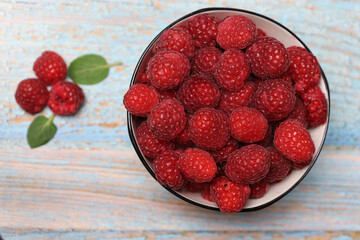 Fresh organic raspberries in a white bowl on a rustic wooden table. Healthy food concept.
