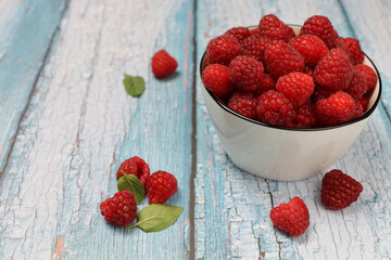 Fresh organic raspberries in a white bowl on a rustic wooden table. Healthy food concept.
