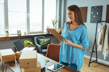 Young online business owner looking at laptop while preparing deliveries for clients. Young woman are preparing a package for delivery to clients. Online clothing store. Small business owners